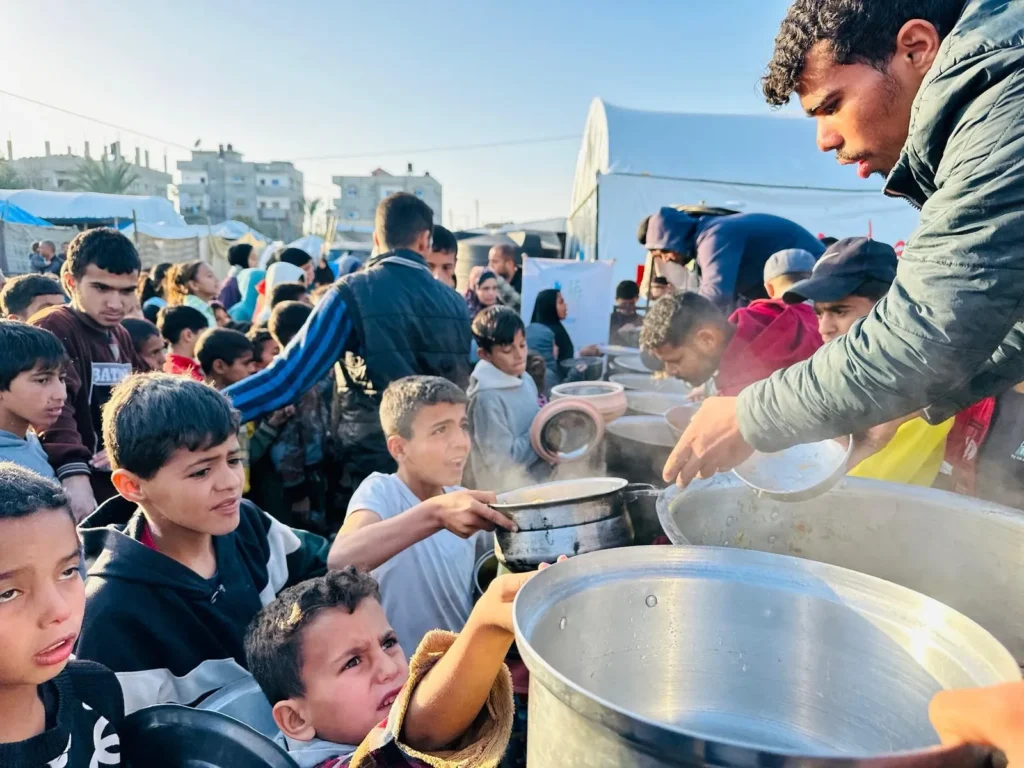 Vrijwilligers delen warme maaltijden uit aan kinderen tijdens een voedseluitdeling in Gaza.