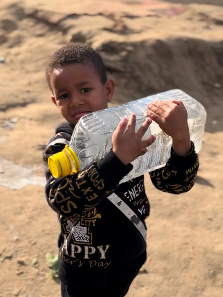 Een jongen houdt een grote lege plastic fles vast in een dorre omgeving, symbool voor watertekort