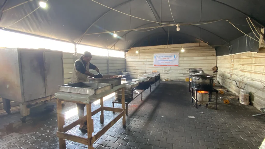 Man bereidt voedsel in een grote kookruimte als onderdeel van een humanitair Aqiqah-project in Gaza
