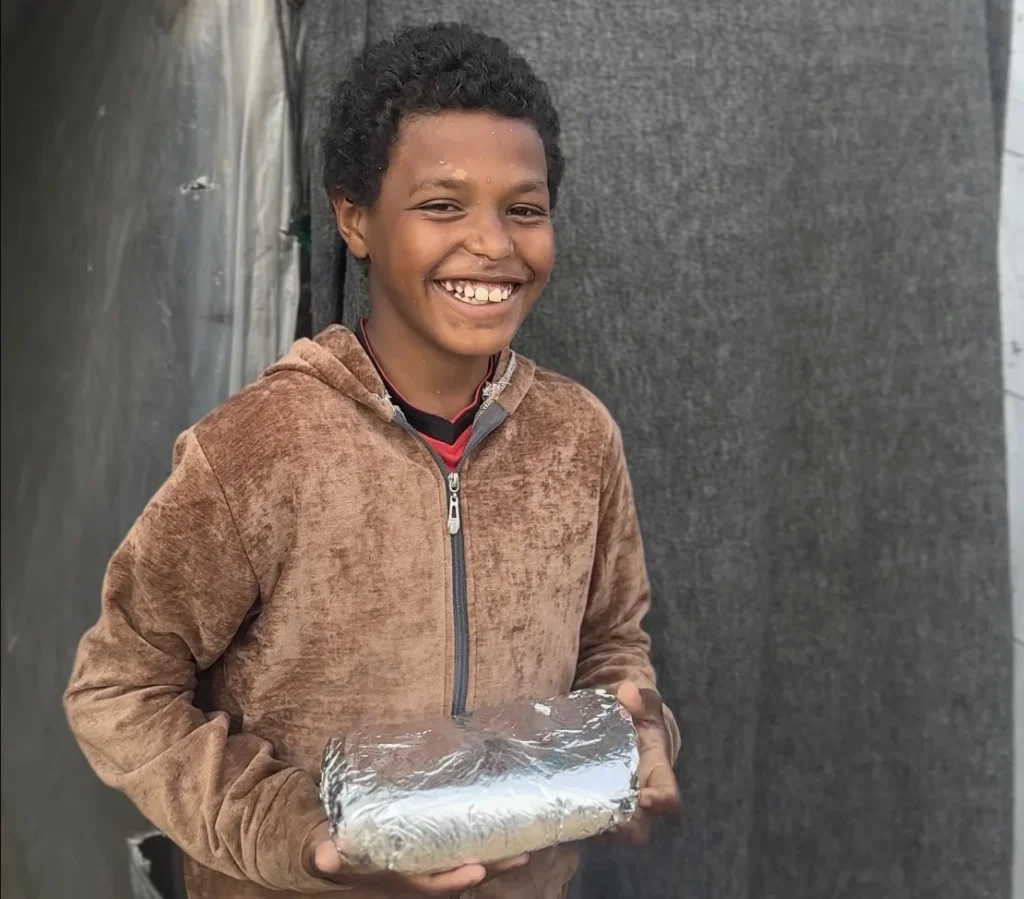 Lachende jongen in bruine hoodie houdt een ingepakt voedselpakket vast