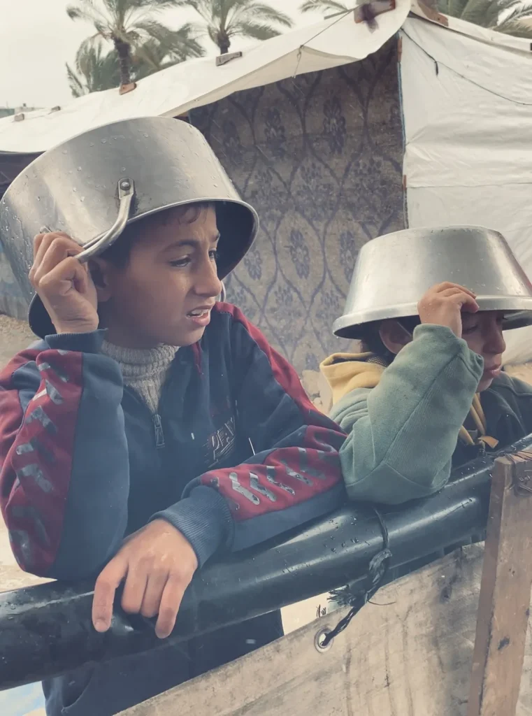 Twee jongens in vluchtelingenkamp in Gaza dragen metalen potten op hun hoofd als bescherming tegen regen