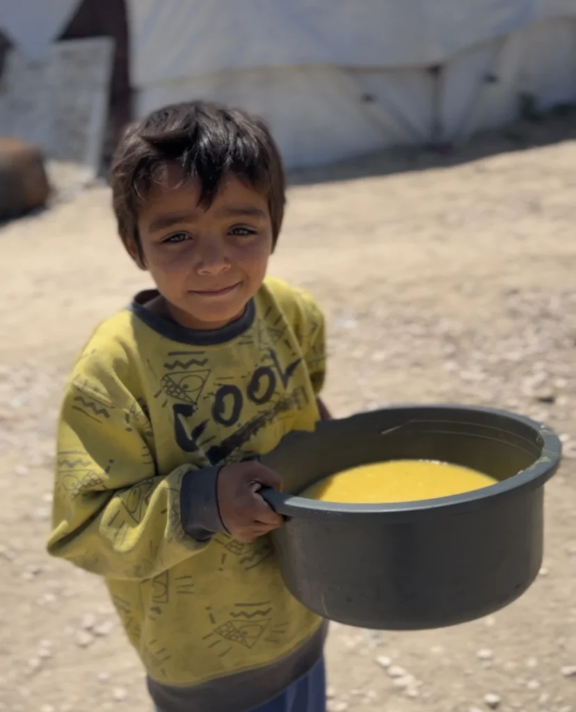Jongen in een vluchtelingenkamp houdt een pan met gele soep vast