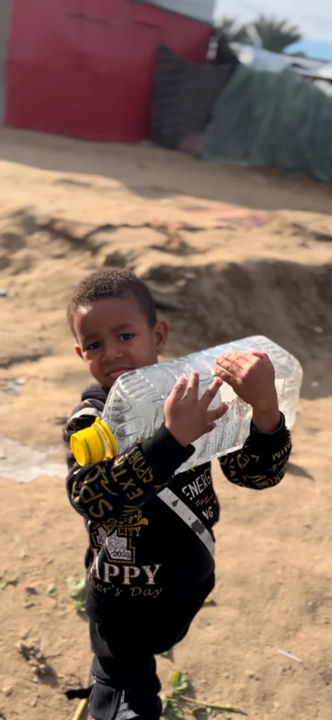 Kind draagt zware plastic waterfles op droge, zanderige ondergrond