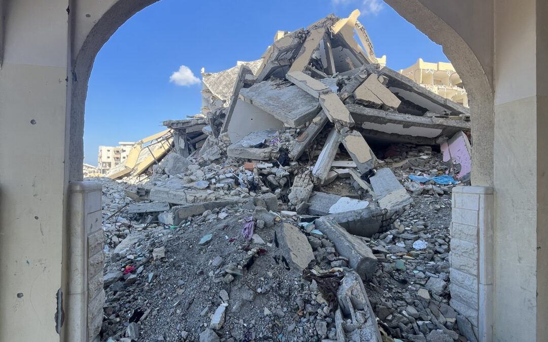 Verwoeste gebouwen en puin in Gaza gezien door een boog, symbool voor noodhulp en wederopbouw van Stichting ULFAH.