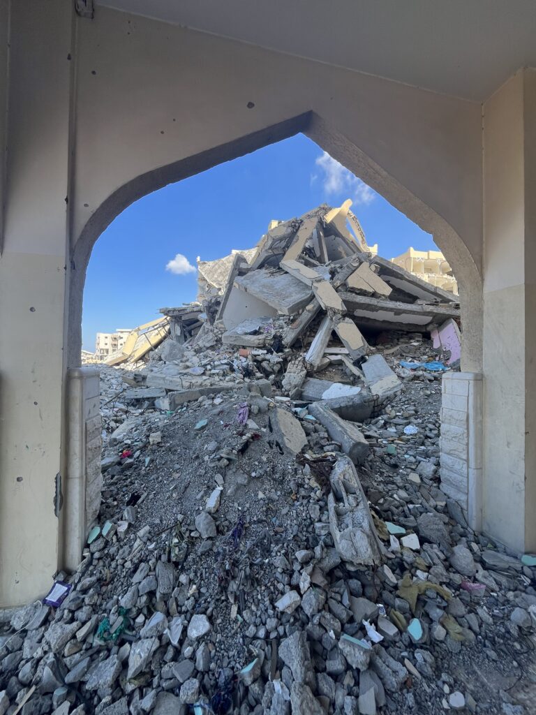Verwoeste gebouwen en puin in Gaza gezien door een boog, symbool voor noodhulp en wederopbouw van Stichting ULFAH.