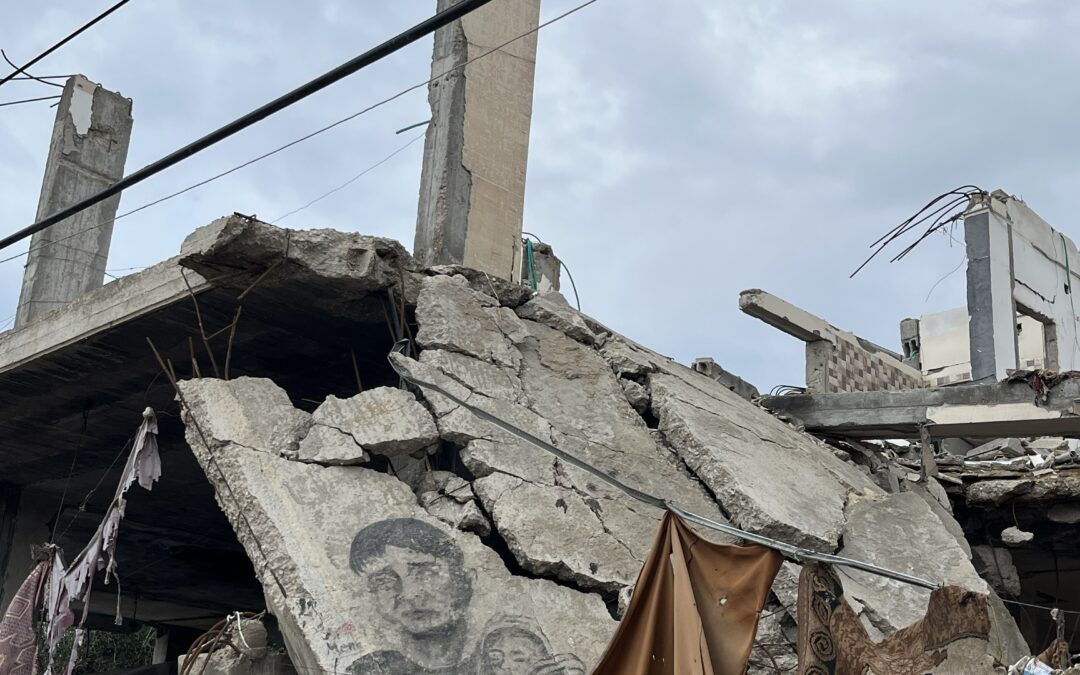Verwoest betonnen gebouw met zichtbaar muurportret van man en kind tussen het puin, onder een bewolkte hemel